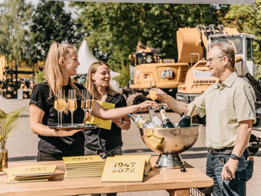 zwei junge Frauen geben einem Mann am Empfang ein Sekt Glas