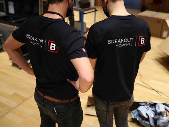 zwei Männer mit Breakout Moments Shirts