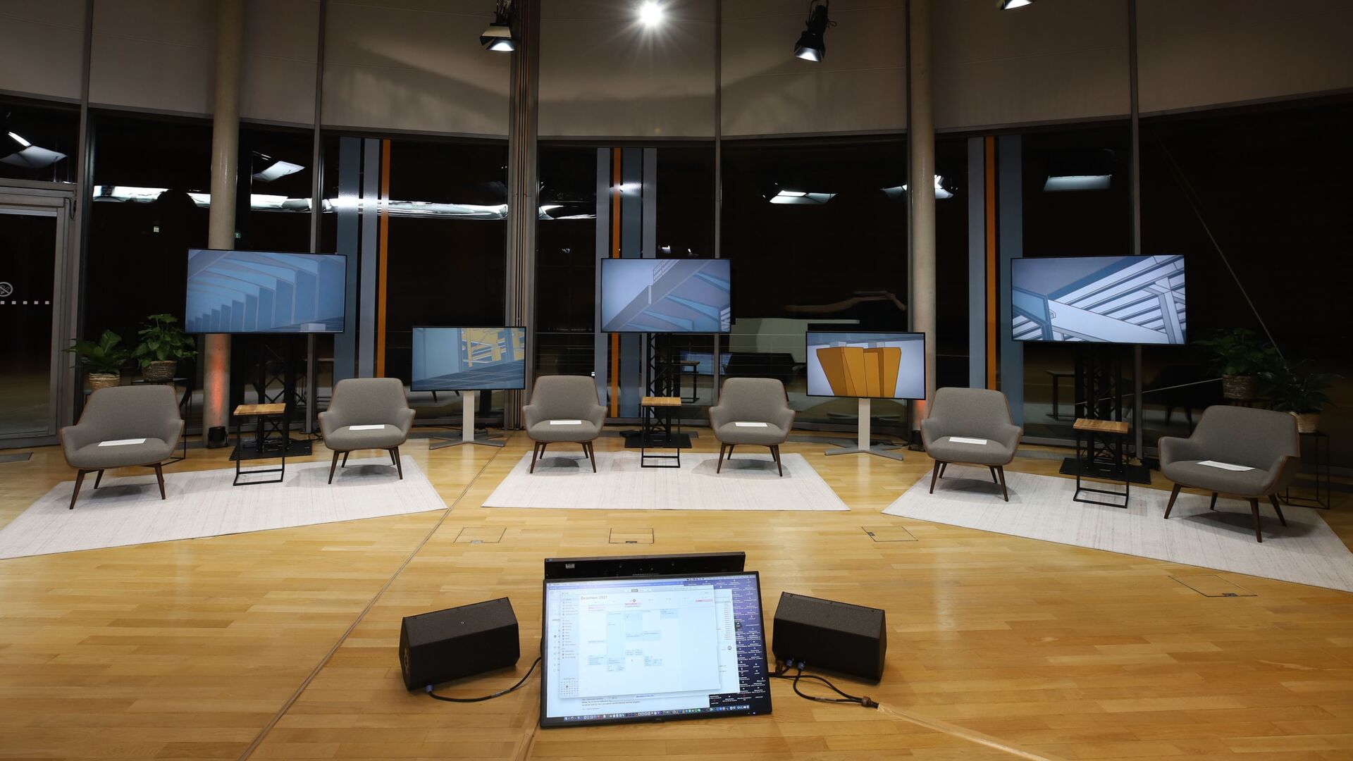 Stuhlreihen vor vielen Bildschirmen für hybride Konferenz