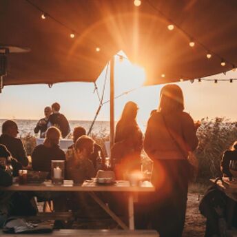 menschen am Meer die zusammen beim Sonnenuntergang essen